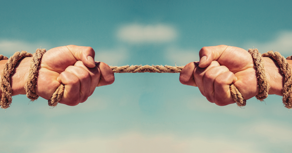 Close-up of two hands with rope around their wrists, each tugging in opposite directions.